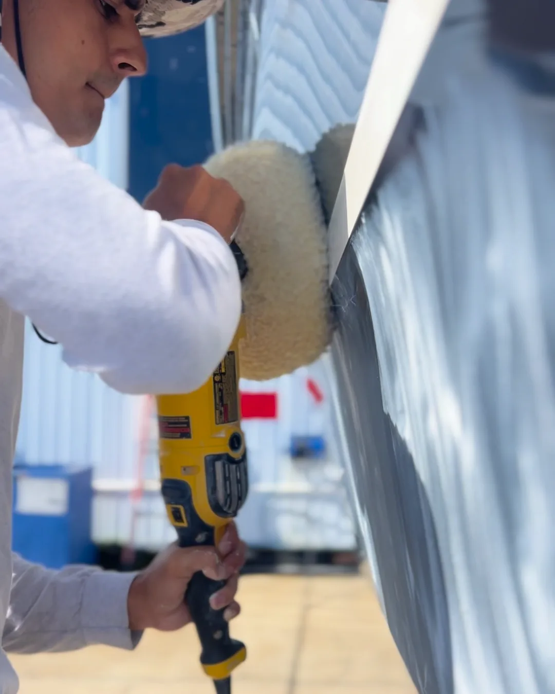 One of the Bayside crew in the sun, working a wool pad along a white hull.