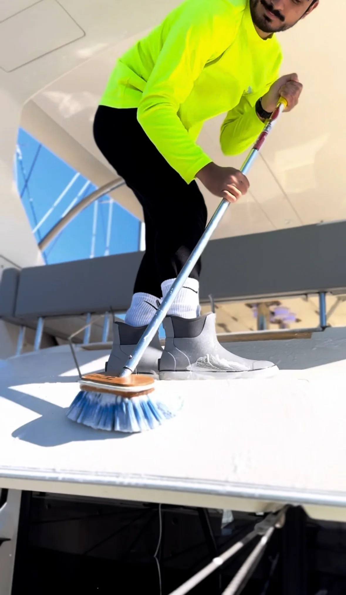 Somebody in deck shoes scrubbing a white boat deck with a long handled brush.