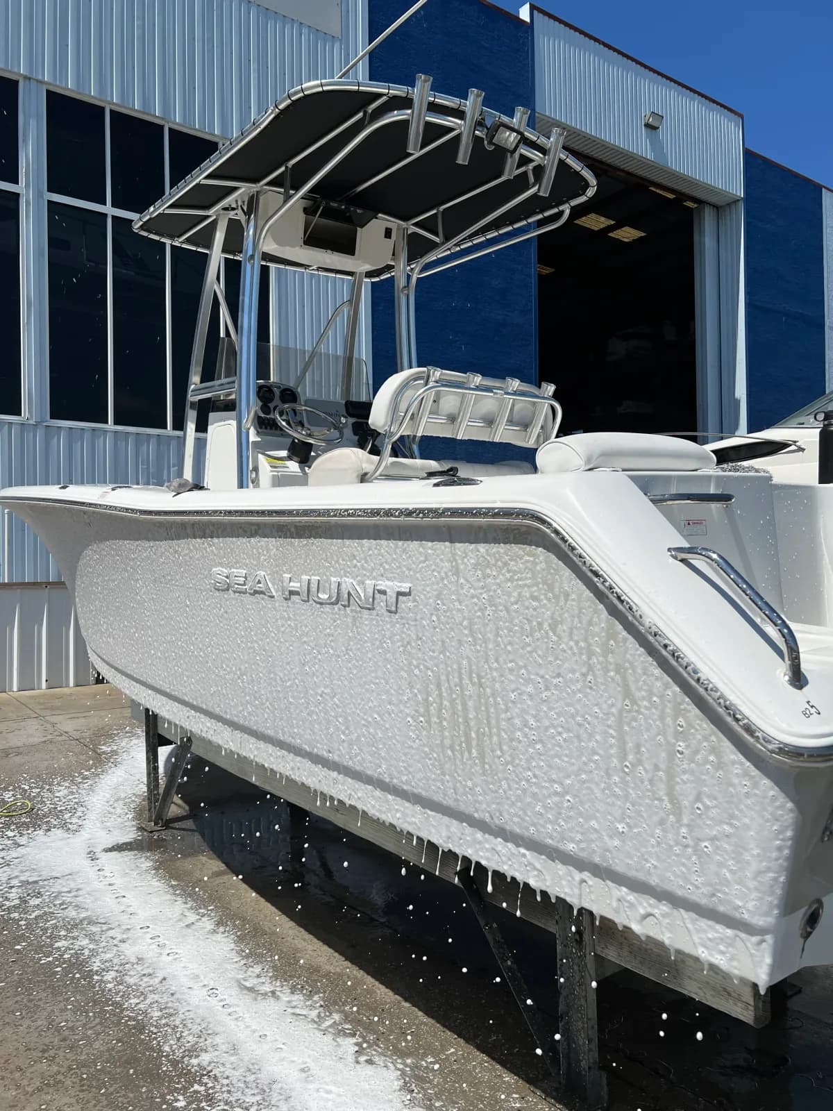 A Sea Hunt center console on a lift mid wash, soap running down the white hull.