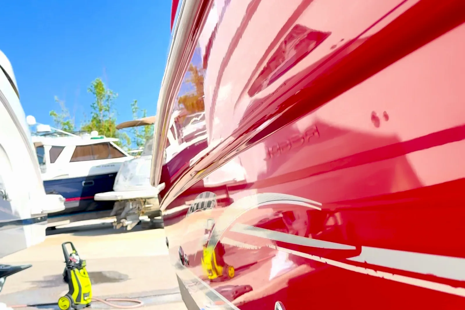 A restored red hull, the sky and the boats in the yard reflected in its gloss.