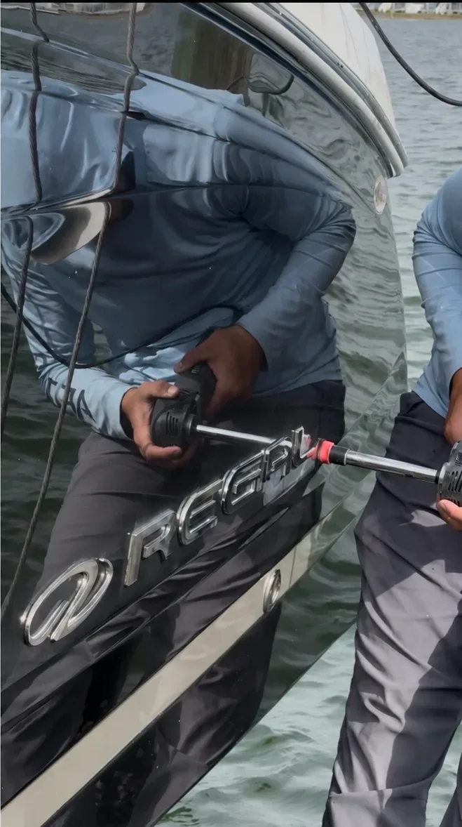 A Bayside technician polishing the transom of a boat in its slip, the crew reflected in the gloss