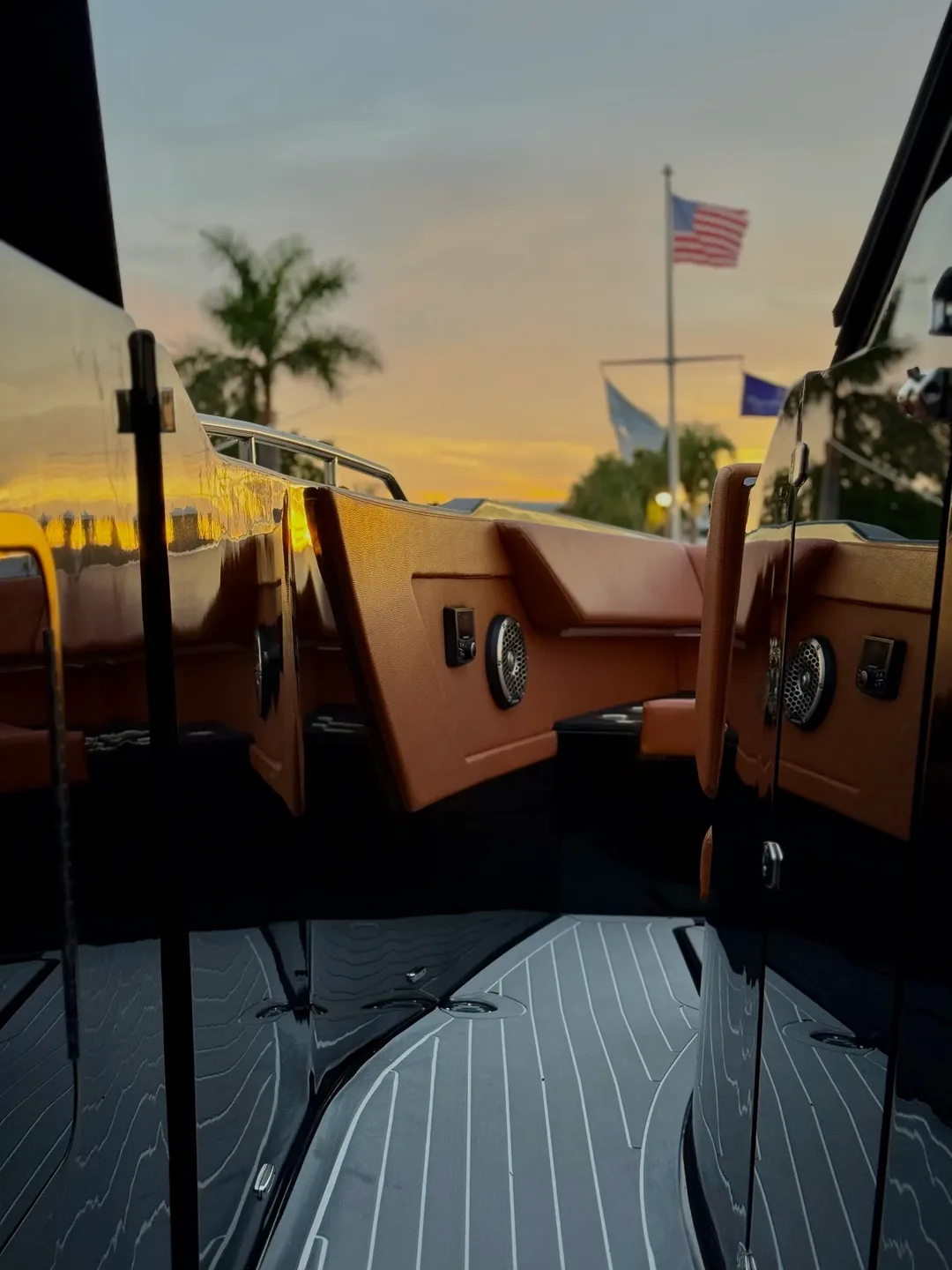 A black hull polished to a mirror, the sunset, a palm and the flag at the marina reflected in it.